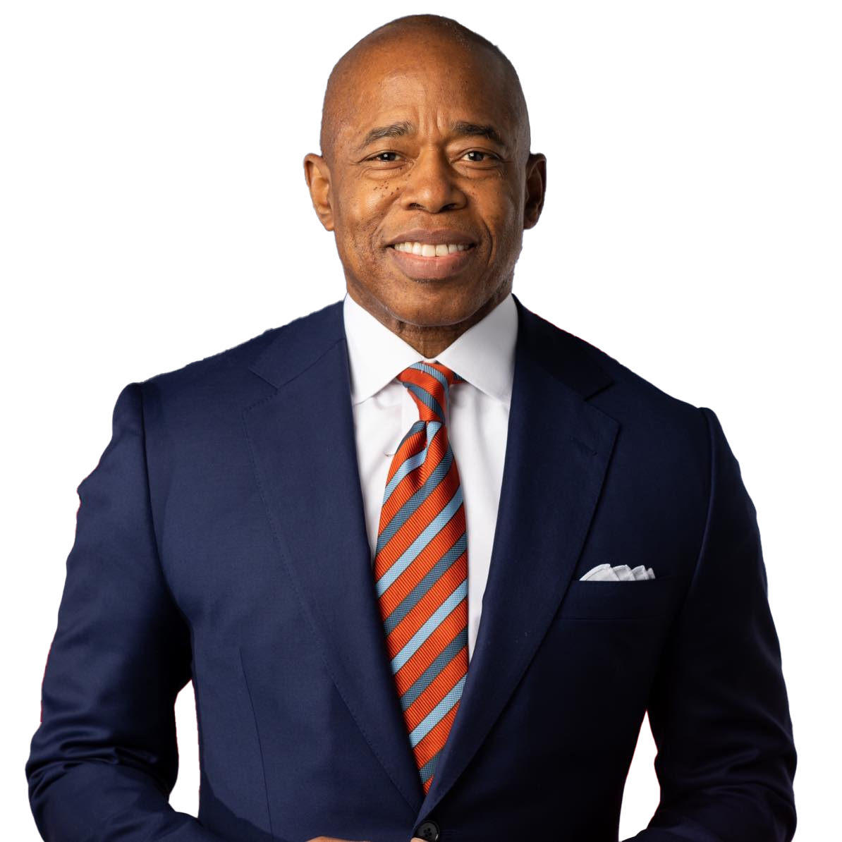 Mayor Eric Adams in a navy suit and red-striped tie stands in front of an American flag and another flag, smiling at the camera. Representing Rise Up NYC, he has a clean-shaven head and a white pocket square. Rise Up NYC