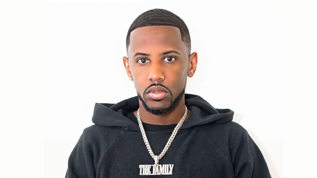 Fabolous with short, neatly styled hair and a trimmed beard wears a black hoodie and a silver chain necklace with a "THE FAMILY" pendant, standing against a plain white background, channeling Lloyd’s signature cool style. Rise Up NYC